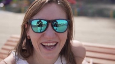 Güneş gözlüklü, gülümseyen bir kadının yakın çekimi.