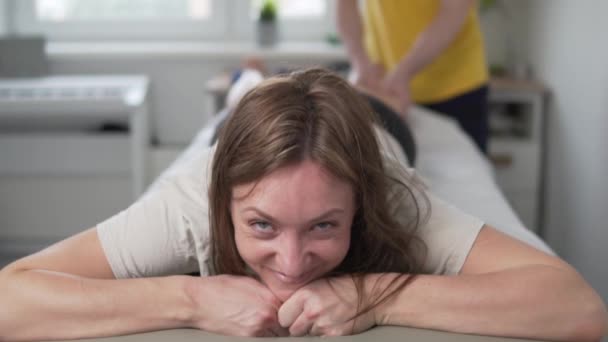 Uma mulher feliz mostra um sinal legal enquanto massageia as pernas em uma mesa de massagem — Vídeo de Stock