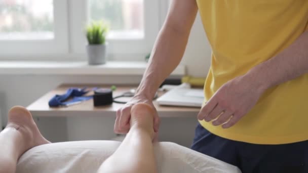 Un masajista masculino masajea los pies de una mujer en casa sobre una mesa de masaje — Vídeo de stock