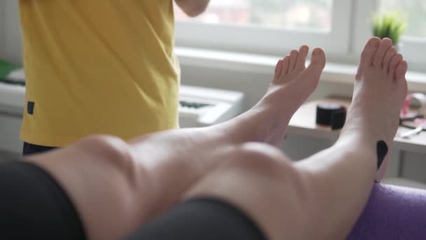 Žena si vyvíjí nohu s instruktorem po operaci doma. — Stock video
