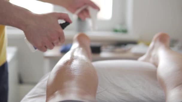 Der Masseur behandelt das Bein des Athleten mit Alkohol und wischt es mit einem Handtuch — Stockvideo