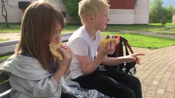Los niños comen comida rápida en el verano en un banco del parque — Vídeos de Stock