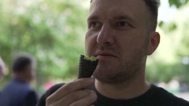 Κοντινό πλάνο, ένας άνθρωπος τρώει παγωτό σε ένα κέρατο βάφλας το καλοκαίρι σε ένα πράσινο πάρκο — Αρχείο Βίντεο
