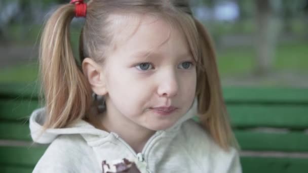 A beautiful little girl eating Eskimo ice cream in a park on the street, close up — Stock Video