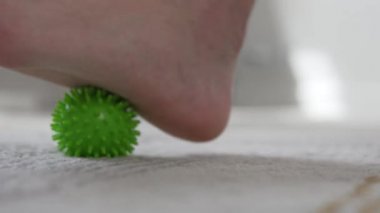 Yakından, adamın biri ayak tabanında dikenler olan bir masaj topunu yuvarlıyor.