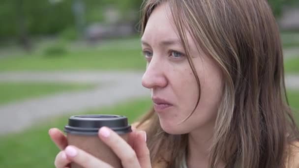 Een mooie vrouw drinkt koffie met haar uit een papieren glas op straat — Stockvideo