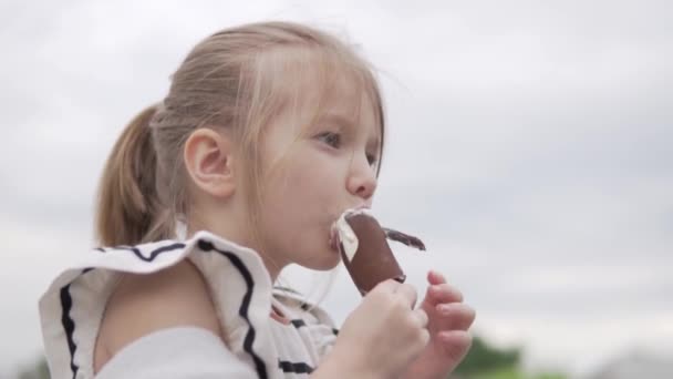 Petite fille drôle mange de la crème glacée sur un bâton en été dans la rue — Video