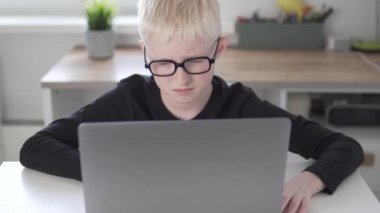 Gözlüklü güzel bir sarışın çocuk bilgisayardan uzaktan öğreniyor.