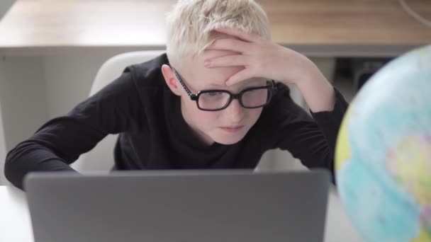 Un niño con gafas para aprender de casa en un ordenador — Vídeo de stock