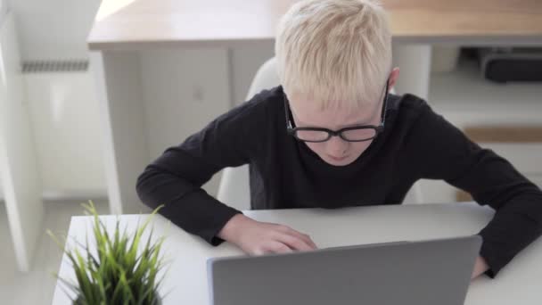 Un niño con gafas aprende a programar en casa detrás de un portátil — Vídeos de Stock