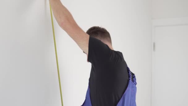 Un costruttore maschio in uniforme misura la distanza desiderata sulla parete prima di riparare — Video Stock