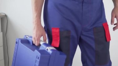 Üzerinde aletler olan mavi bir bavul taşıyan üniformalı bir işçi. Elinde bir bavul taşıyor.