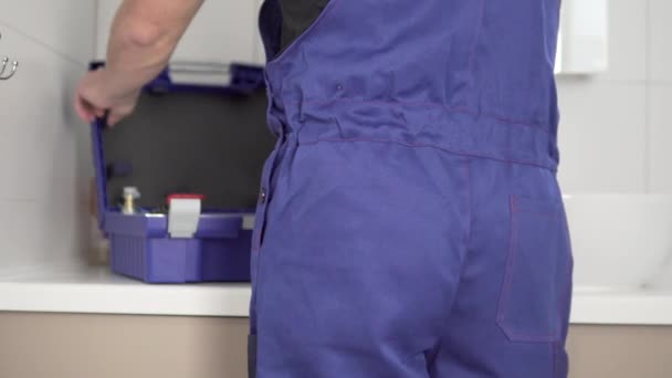 View from the back, a man in a plumbing suit pulls tools from a work suitcase — Stock Video