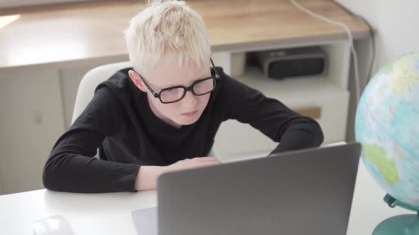 Un chico con gafas está sentado en la computadora en casa. — Vídeos de Stock