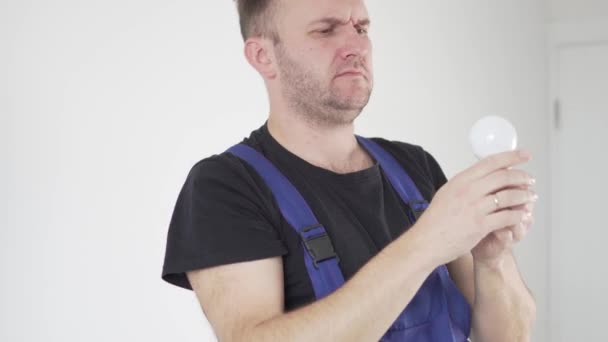 Um eletricista masculino em uniforme torce uma lâmpada em um lustre no teto — Vídeo de Stock