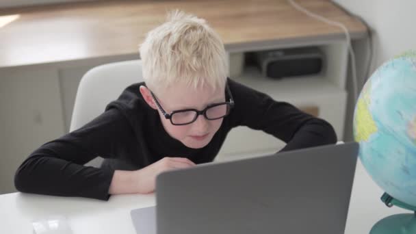 En pojke skolpojke är förlovad hemifrån på en dator — Stockvideo