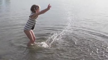 Yavaş çekim, mutlu küçük bir kız gün batımında suya düşer..