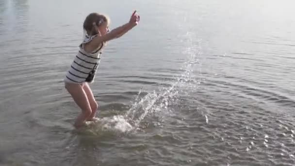 Slow-motion skytte, en glad liten flicka stänk i vattnet vid solnedgången. — Stockvideo