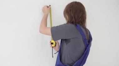 Bir kadın duvarda ölçü alır, rulet santimetre kullanır.