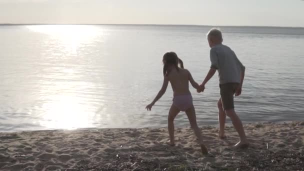 Kinderen rennen in het water hand in hand in de zomer bij zonsondergang — Stockvideo