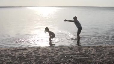 Gün batımında gölde oynayan çocuklar. Erkek ve kız kardeş yazın suya su sıçratır.