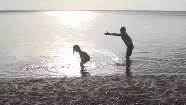 Niños jugando en el lago al atardecer. Hermano y hermana chapotean en el agua en verano — Vídeo de stock