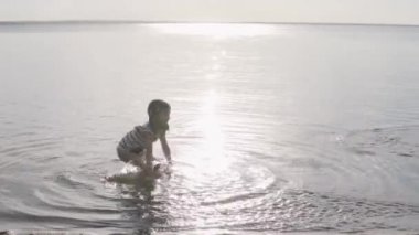 Küçük bir kız yazın gün batımında göle girer ve su sıçratır.