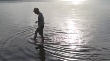 Rusya 'da yazın gün batımında bir çocuk gölde yürür.