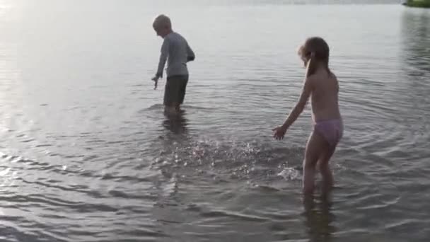 Дети играют в воде озера на закате, красивый противотуманный свет — стоковое видео