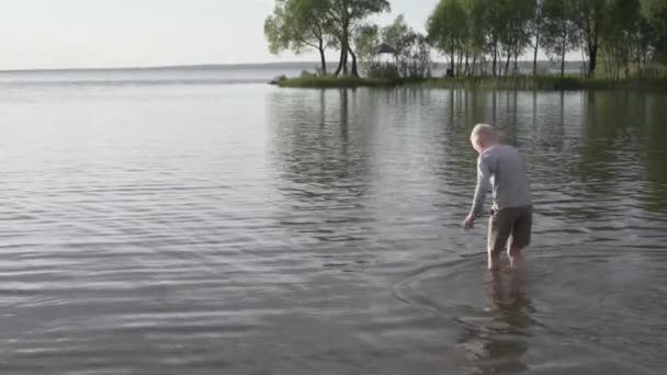 Un niño camina por el lago en el verano. — Vídeo de stock
