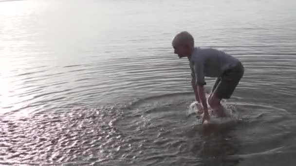 Egy fiú vizet fröcsköl a tóba naplementekor.. — Stock videók