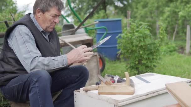 An elderly man makes a wooden box at the cottage in the summer — Stock Video