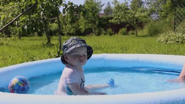 Małe dziecko siedzi w basenie dla dzieci z wodą w upalny letni dzień — Wideo stockowe