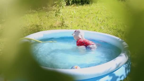 Widok zza krzaka, dziecko pluska w basenie dla dzieci w lecie w parku — Wideo stockowe