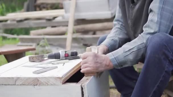 Yaşlı bir adam yazın kır evinde tahta kesiyor. — Stok video