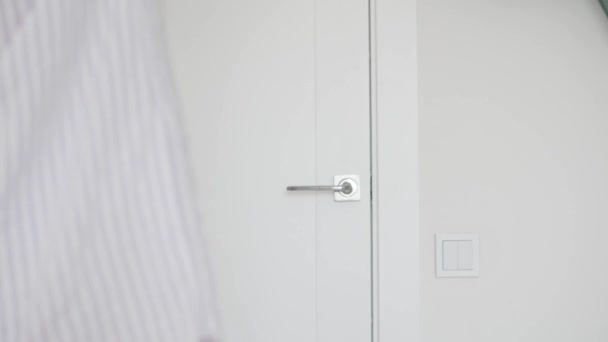 Uma mulher em uma camisa abre a porta branca para o quarto pelo punho e sai — Vídeo de Stock