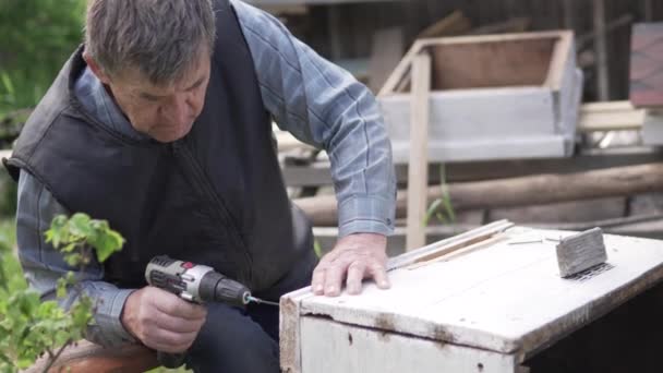 Um homem idoso recolhe uma casa para abelhas no verão na trama — Vídeo de Stock