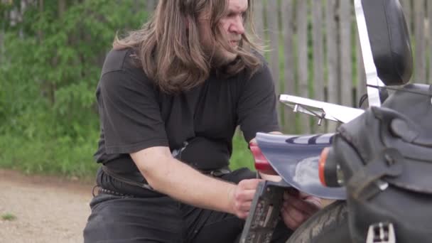 Brutal man bike repairs his motorcycle in the summer on the street — Stock Video