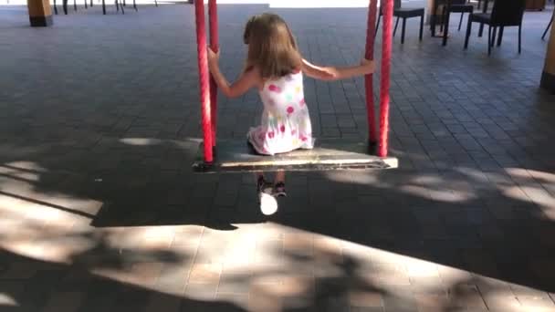 Маленькая девочка катается на качелях летом в парке, вид сзади — стоковое видео
