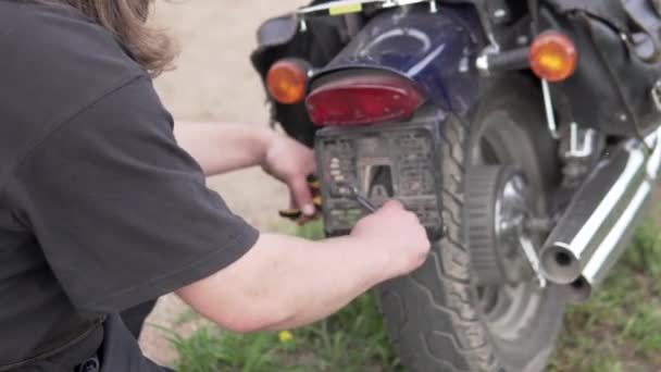 A man screws the frame for the number on a motorcycle — Stock Video