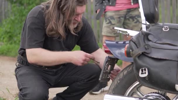 En motorcyklist reparerar sin cykel på sommaren på gatan — Stockvideo