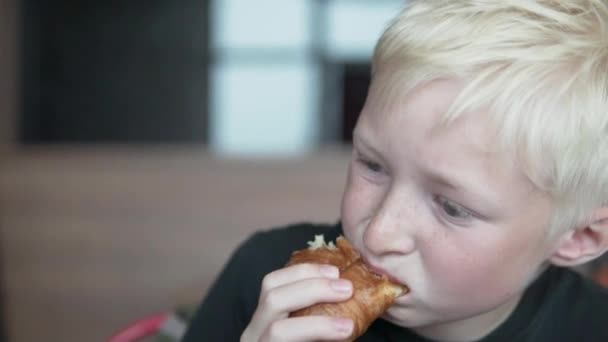 Lindo menino loira come um sanduíche em um café sozinho — Vídeo de Stock