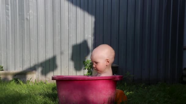 Un bambino carino si siede in estate in un bacino con acqua sull'erba verde — Video Stock
