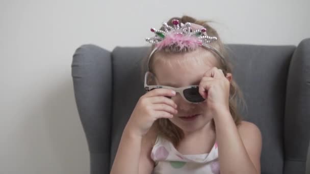 Een klein meisje in een speelgoedkroon draagt een zonnebril — Stockvideo