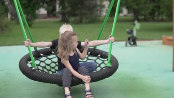 Брат и сестра катаются на качелях в парке летом — стоковое видео