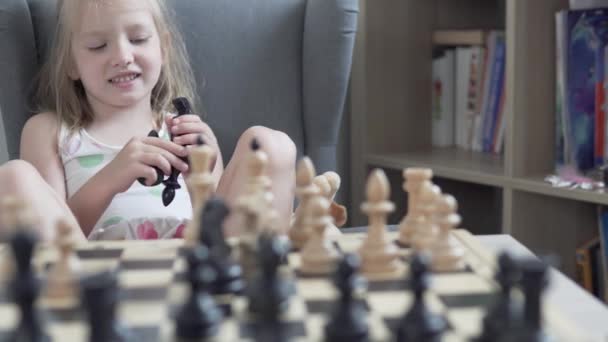 Uma menina bonita aprende a jogar xadrez em casa — Vídeo de Stock