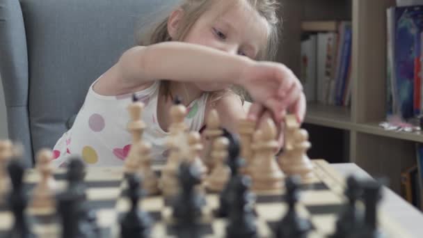 En liten flicka lär sig spela schack hemma med sin pappa, närbild — Stockvideo