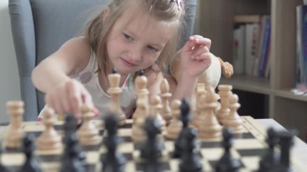 Ein kleines Mädchen mit Plüschtier lernt während einer Quarantäne zu Hause Schach spielen — Stockvideo