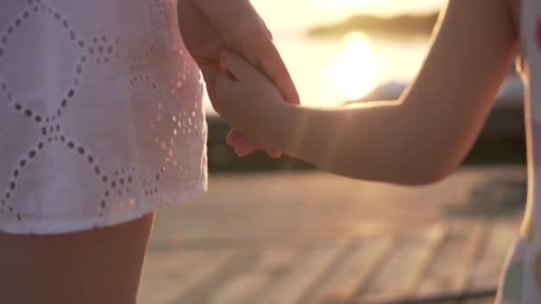 Close-up, de moeder houdt een kleine meisjes hand bij zonsondergang bij de rivier in de zomer — Stockvideo