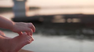 Çocuk gün batımında nehirde ayak parmaklarına dokunur.